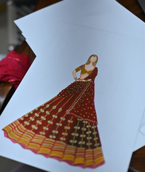 A lehenga drawn out in red and gold on the design desk