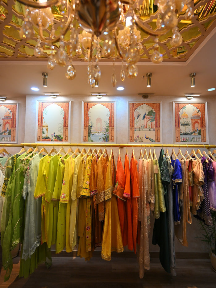 A chandelier hanging above a rail of citrus and green outfits