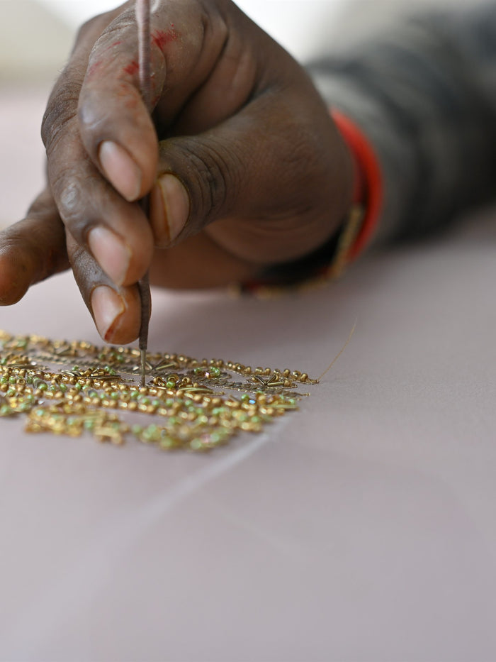 Gold zardozi being laid by hand onto blush fabric