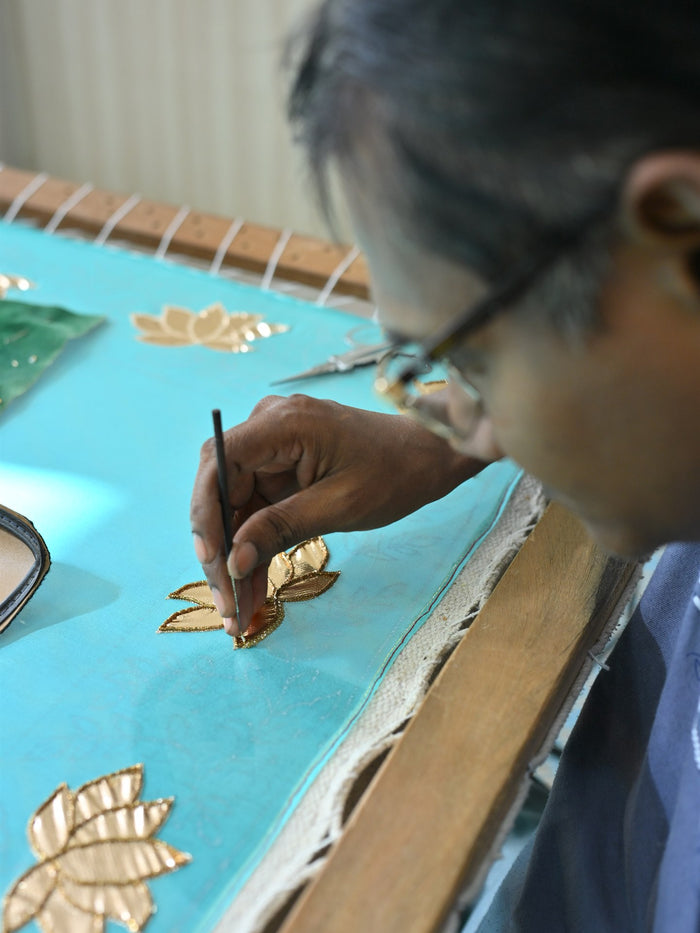 An artisan drawing gold motifs onto turquoise silk